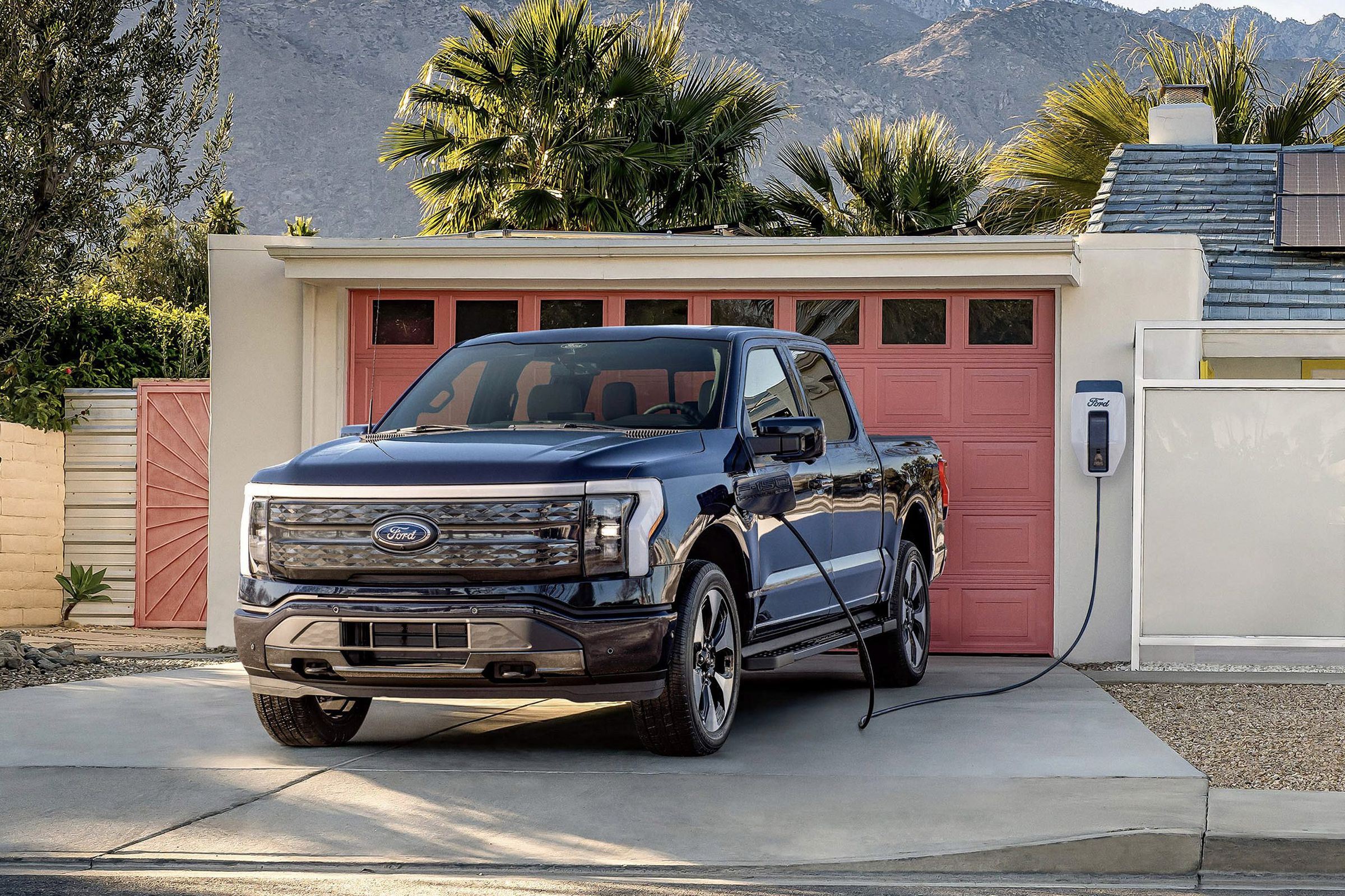 f-150 lightning truck in front of a garage with red door, attached to house with solar panels, and mountain background