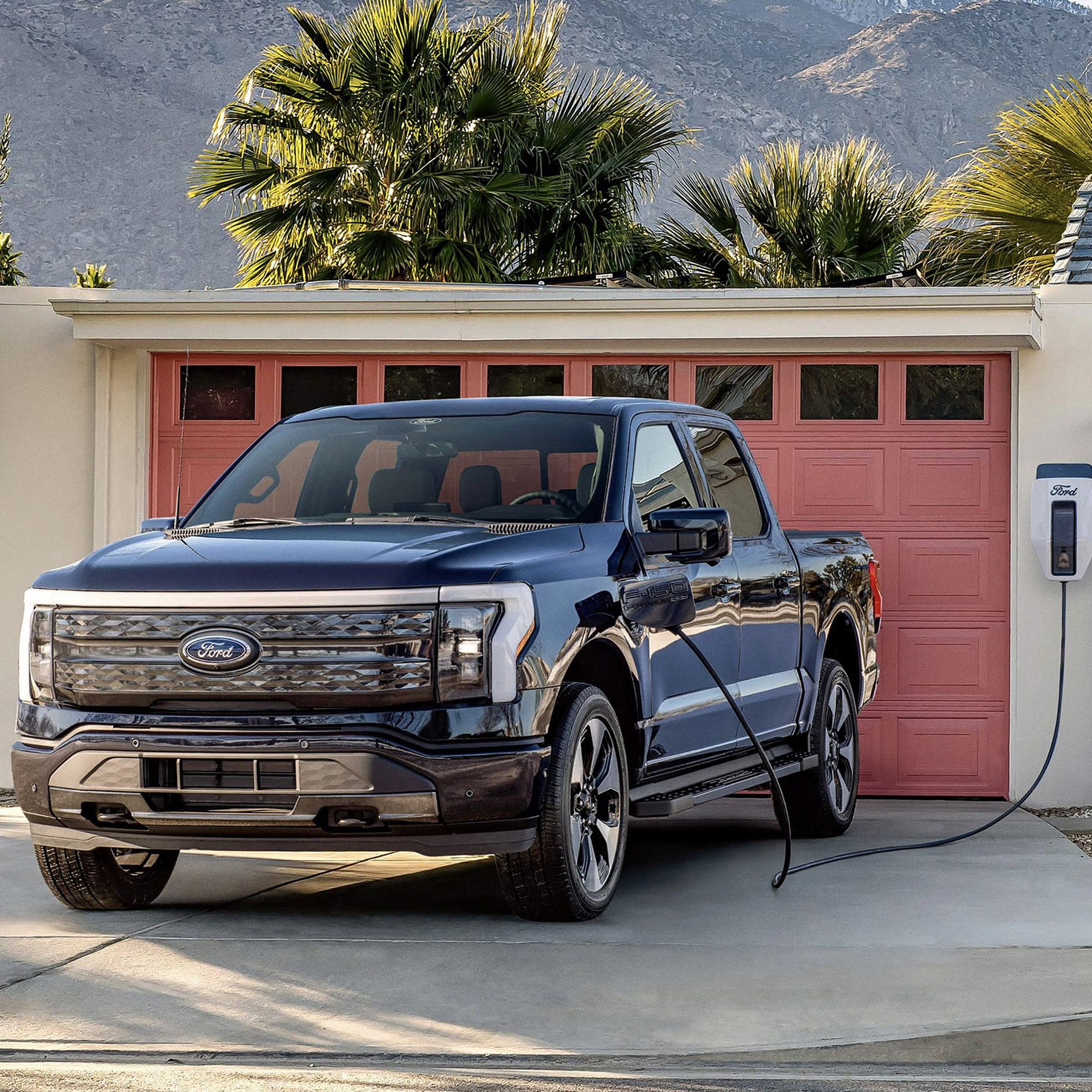 f-150 lightning truck in front of a garage with red door, attached to house with solar panels, and mountain background