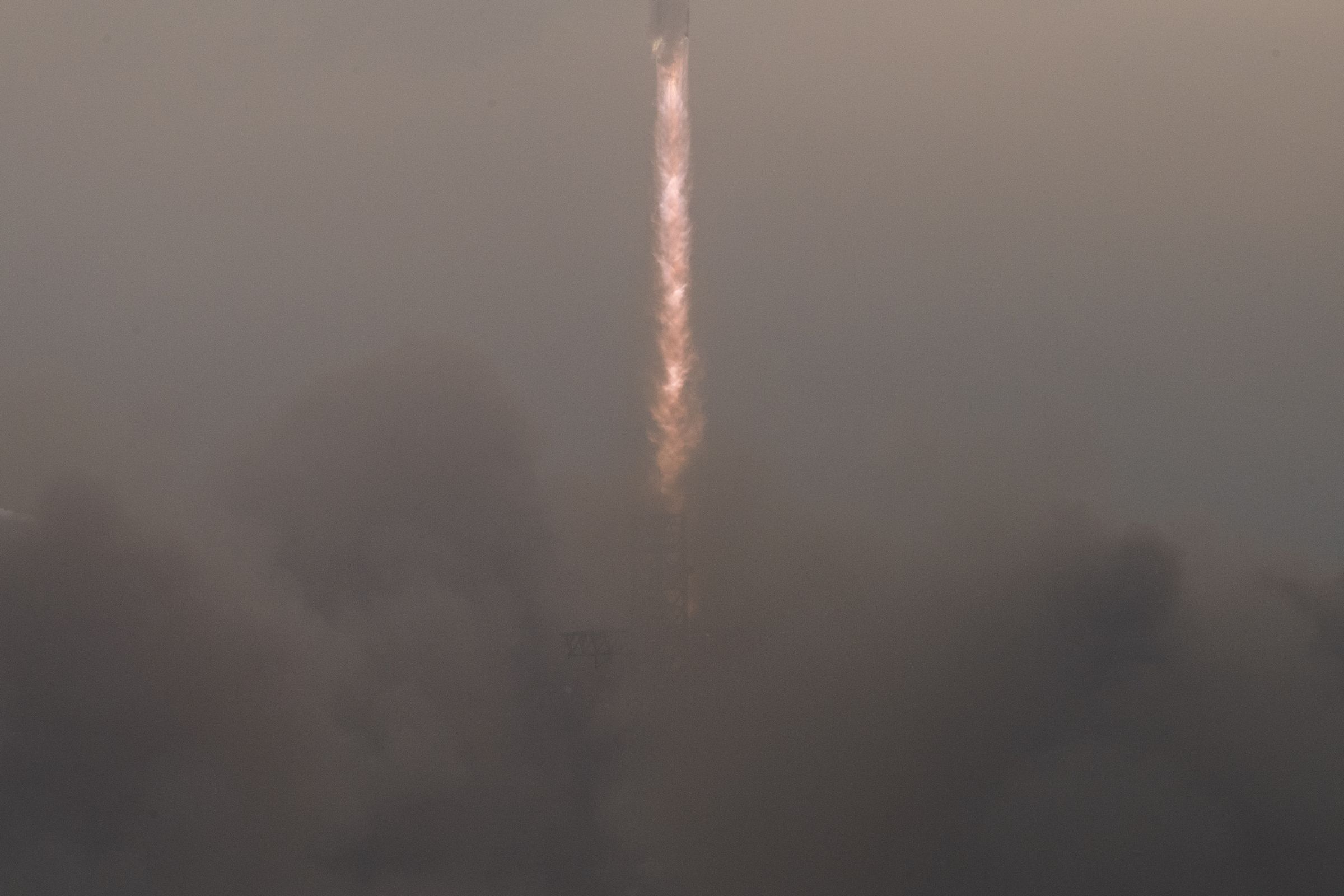 A large plume of dust scene below the fiery tail of a rocket rising.