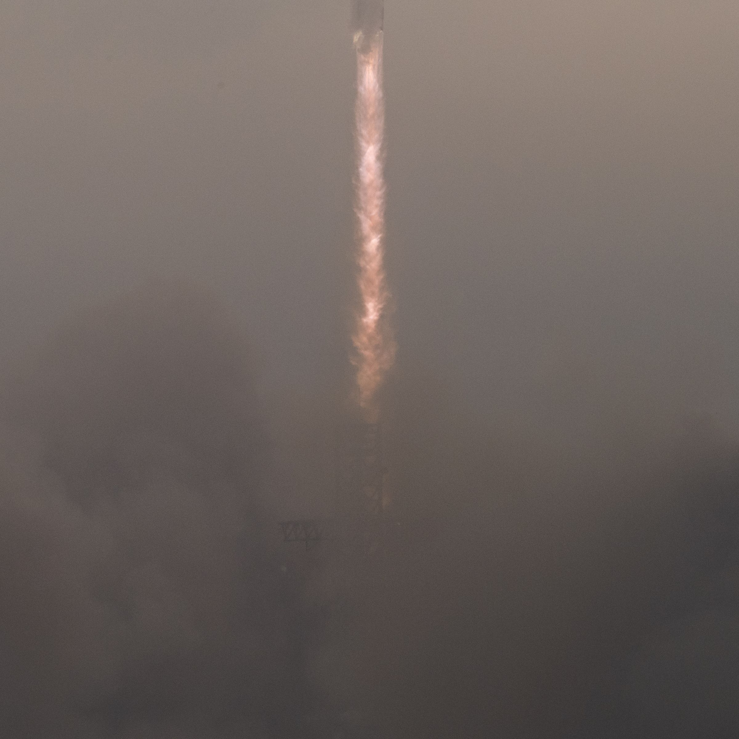 A large plume of dust scene below the fiery tail of a rocket rising.