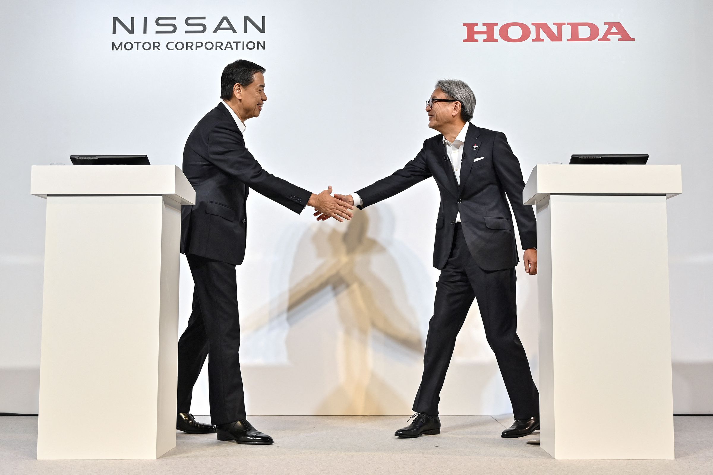 Makoto Uchida (L), president and CEO of Japanese auto maker Nissan, and Toshihiro Mibe (R), director, president and representative executive officer of auto maker Honda, shake hands at the start of in a press conference in Tokyo on August 1, 2024.