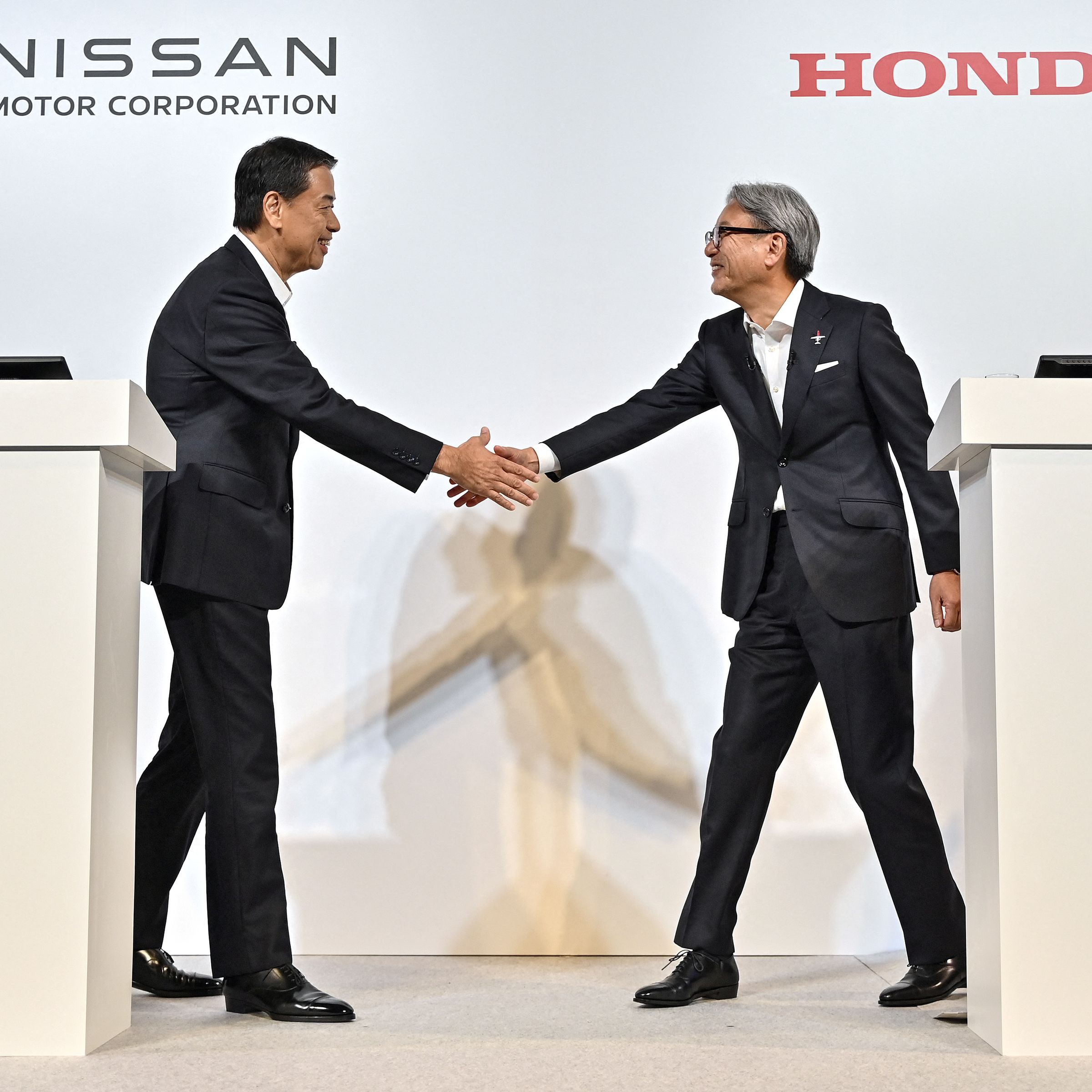 Makoto Uchida (L), president and CEO of Japanese auto maker Nissan, and Toshihiro Mibe (R), director, president and representative executive officer of auto maker Honda, shake hands at the start of in a press conference in Tokyo on August 1, 2024.