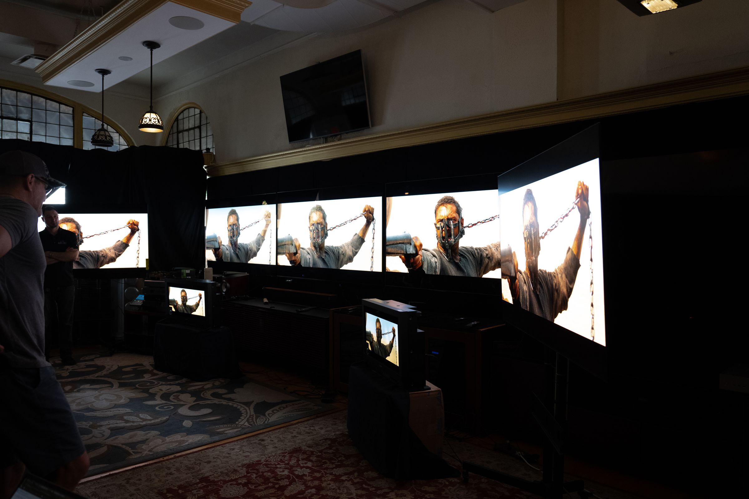 Several large TVs in a dark room showing a scene from Mad Max: Fury Road