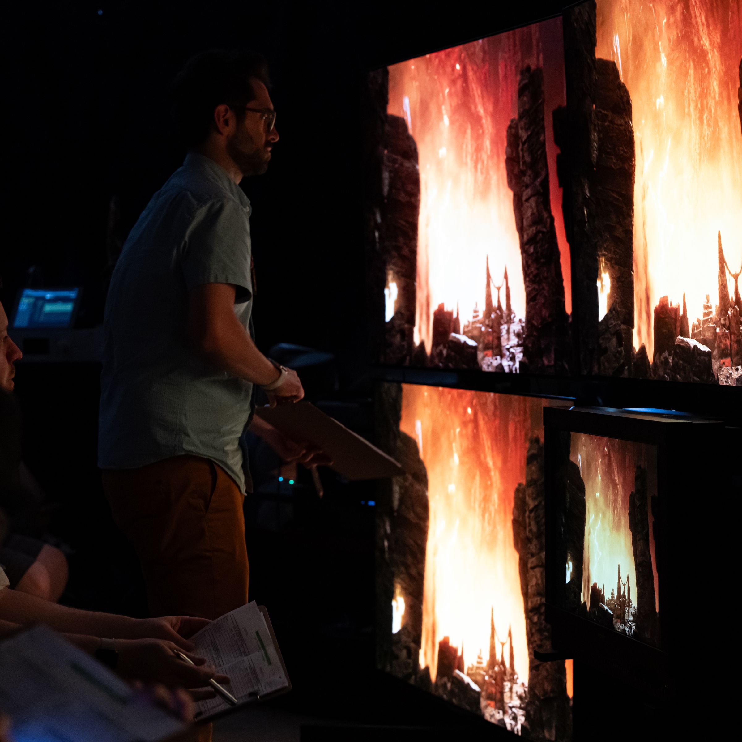 A man looks at several large TVs showing movie scene with bright flames