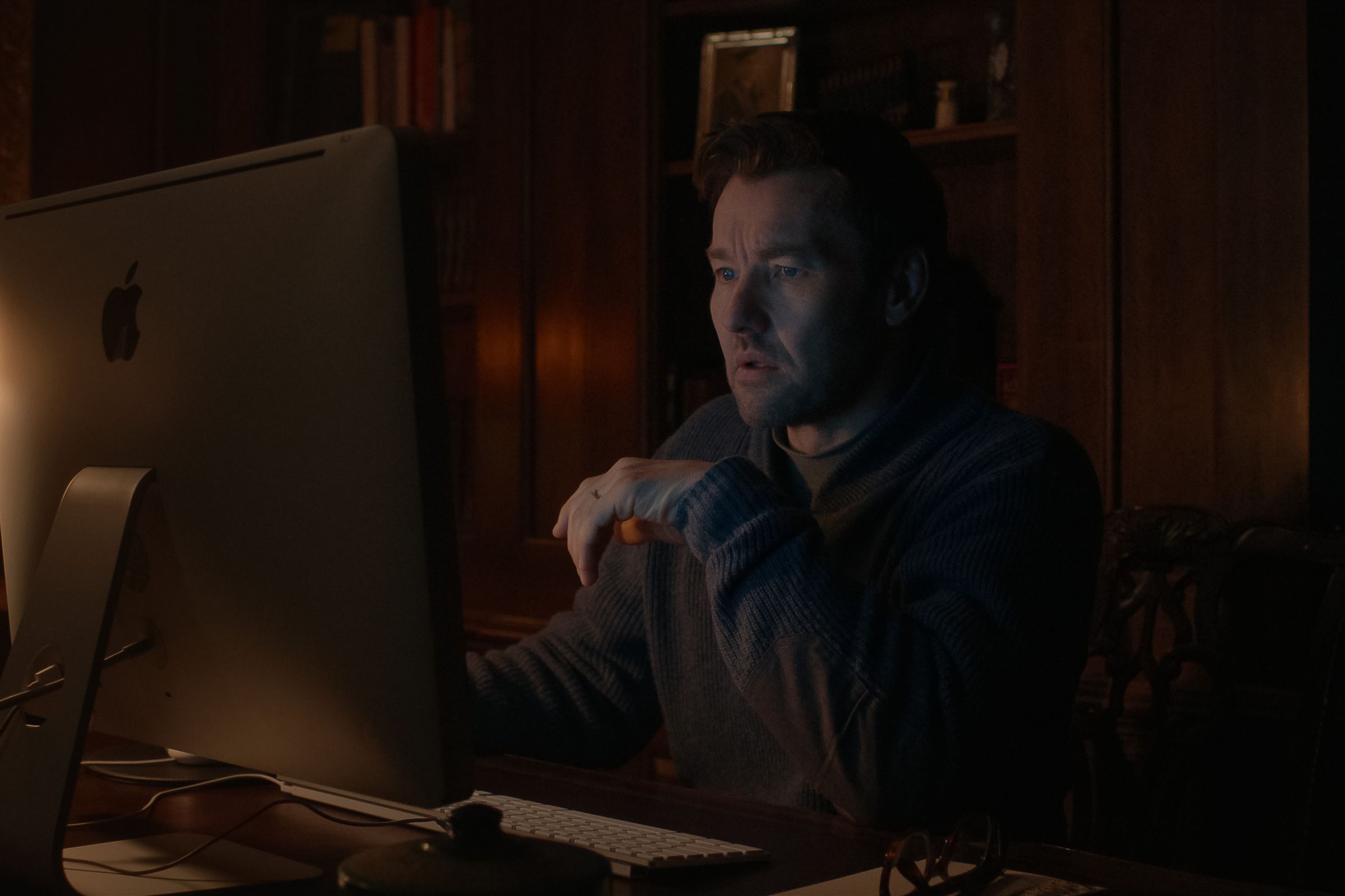 A man sitting in a dark room in front of his computer at a desk.