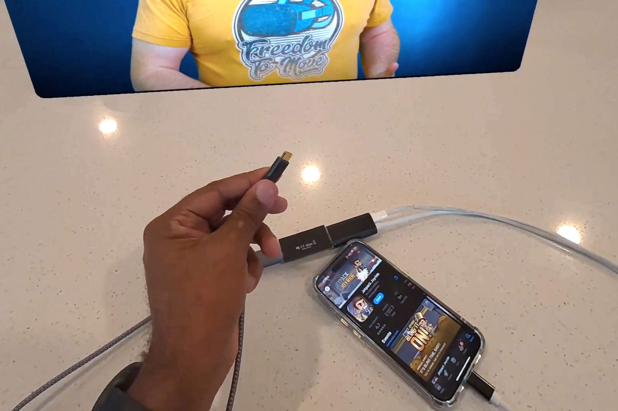 A capture card connected to a smartphone sitting on a table with a virtual screen visible in the background.